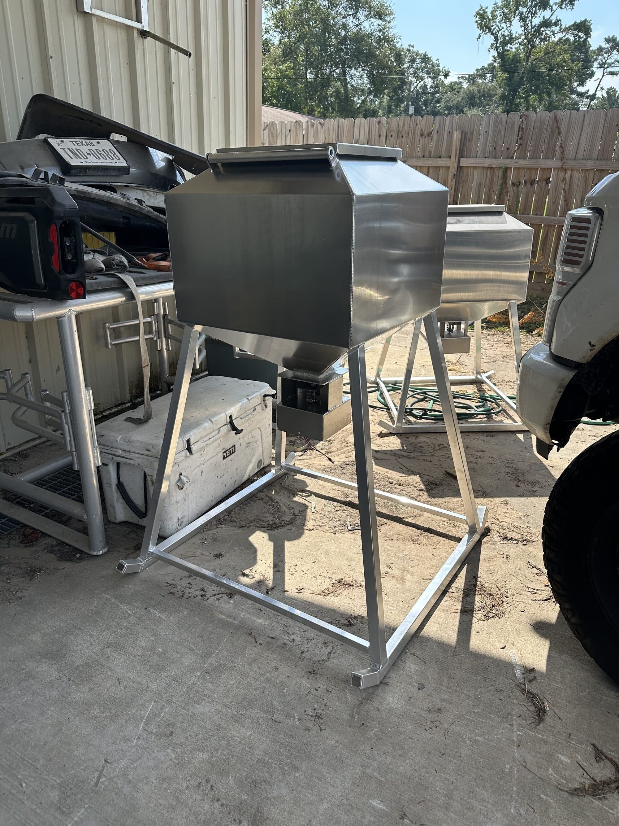 Aluminum fish feeder on a welded stand, hopper and directional dispenser below, at the New Caney shop.